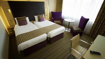 Een hotelkamer met twee bedden, een kleintje tafeltje, een stoel en een bureau met een afstandsbediening.