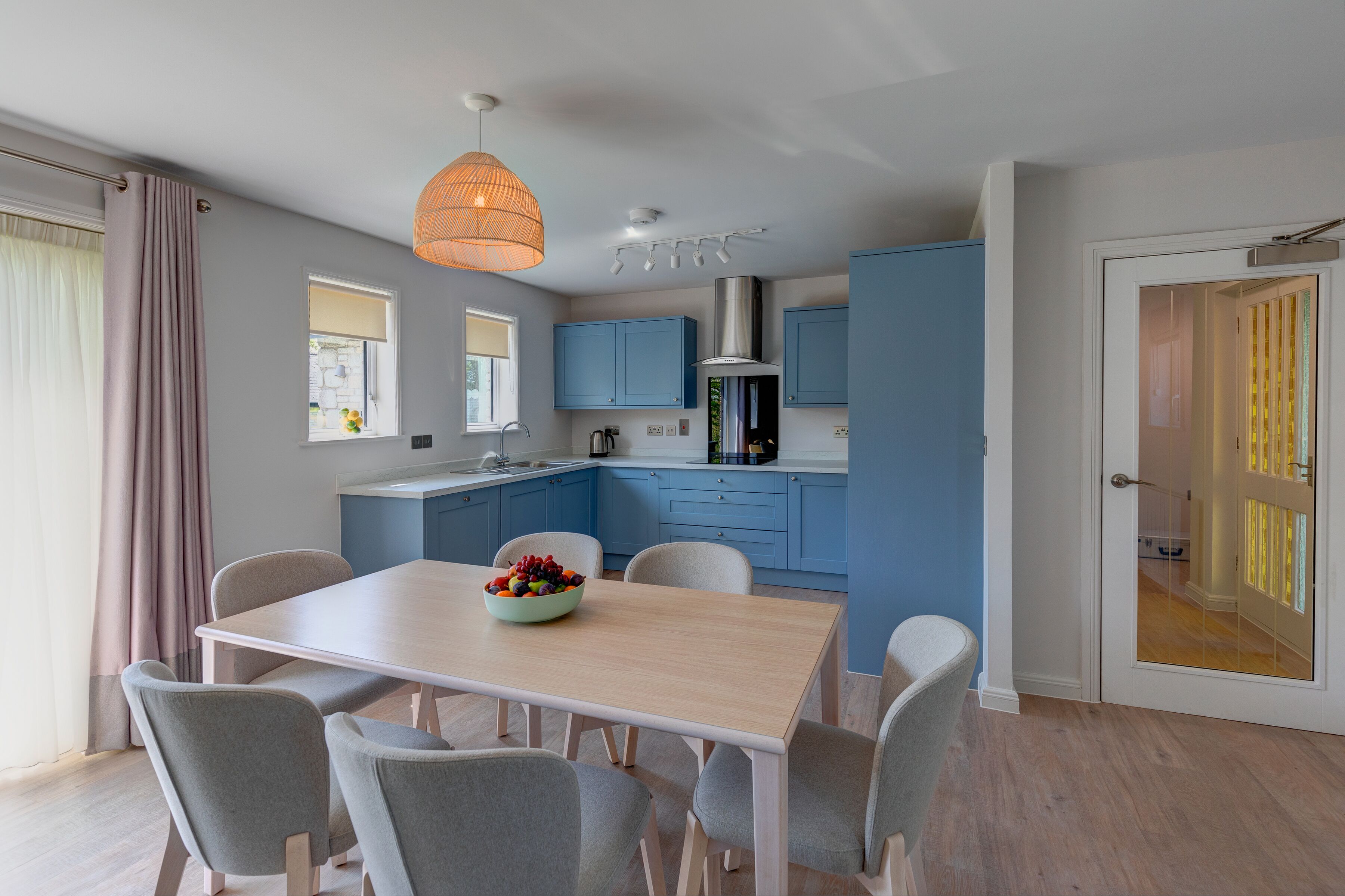Une cuisine moderne avec des meubles bleus, un plan de travail blanc et un coin repas comprenant une table et des chaises en bois.