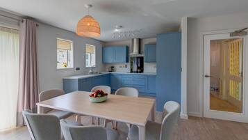 Une cuisine moderne avec des meubles bleus, un plan de travail blanc et un coin repas comprenant une table et des chaises en bois.