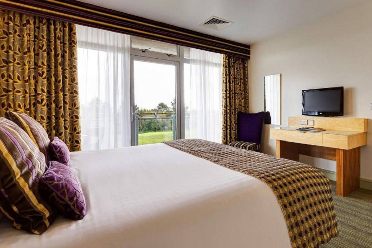Habitación de hotel con una cama grande, un escritorio y televisión, y vistas al exterior.