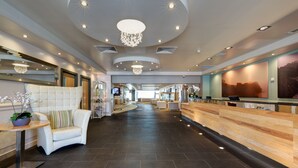 A modern hotel lobby with a reception desk, seating area, and a chandelier.
