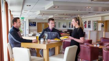 Een restaurant met houten tafels en stoelen, een aan de muur bevestigde televisie en een buffet.