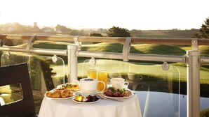 A table set with breakfast items and a glass of orange juice, overlooking a golf course.