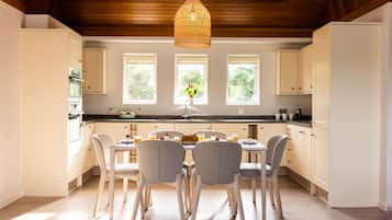 Una cocina moderna con armarios blancos, techo de madera y un comedor con cuatro sillas y una mesa dispuesta para el desayuno.