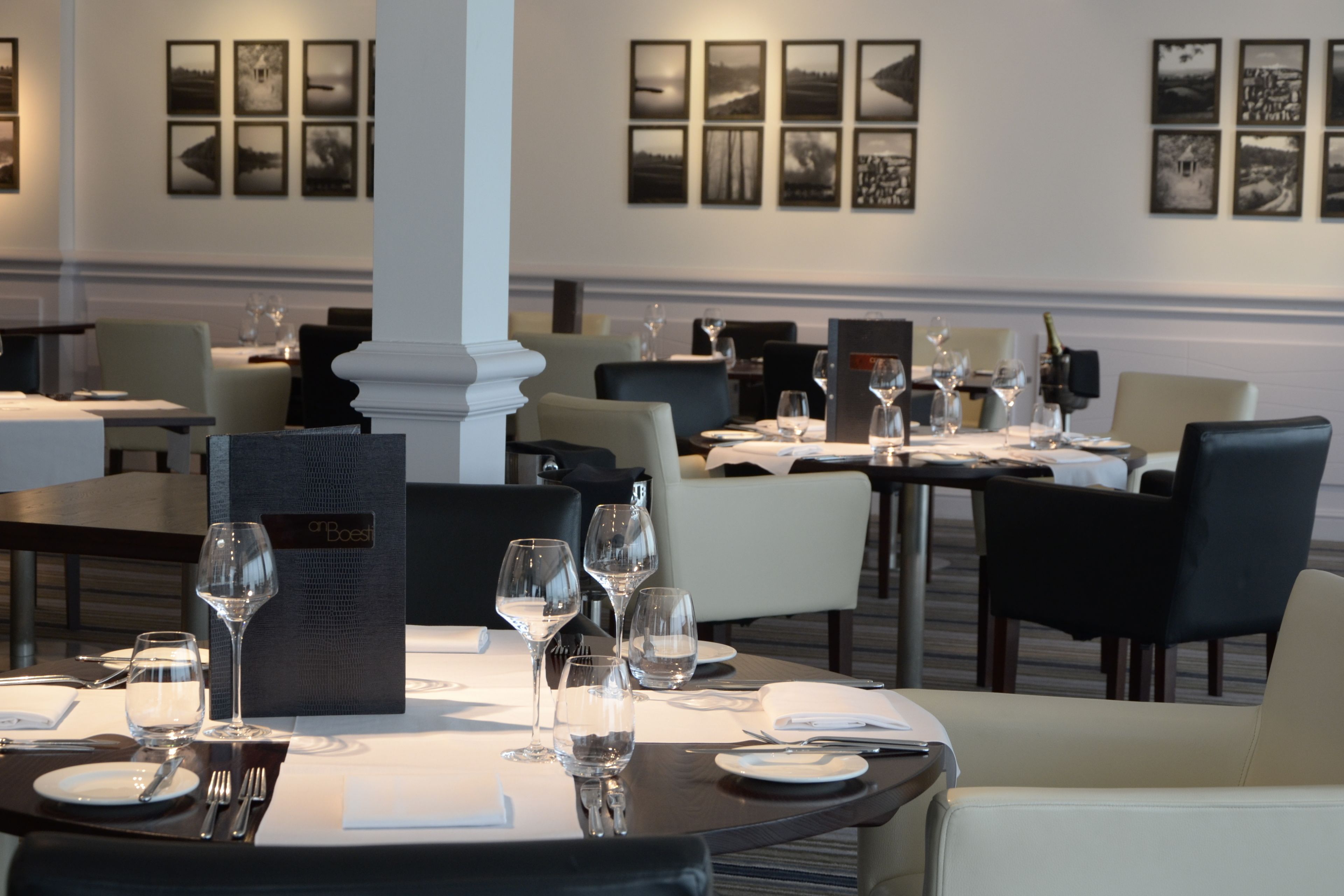 A restaurant with tables set for dining, framed pictures on the wall, and a menu stand.