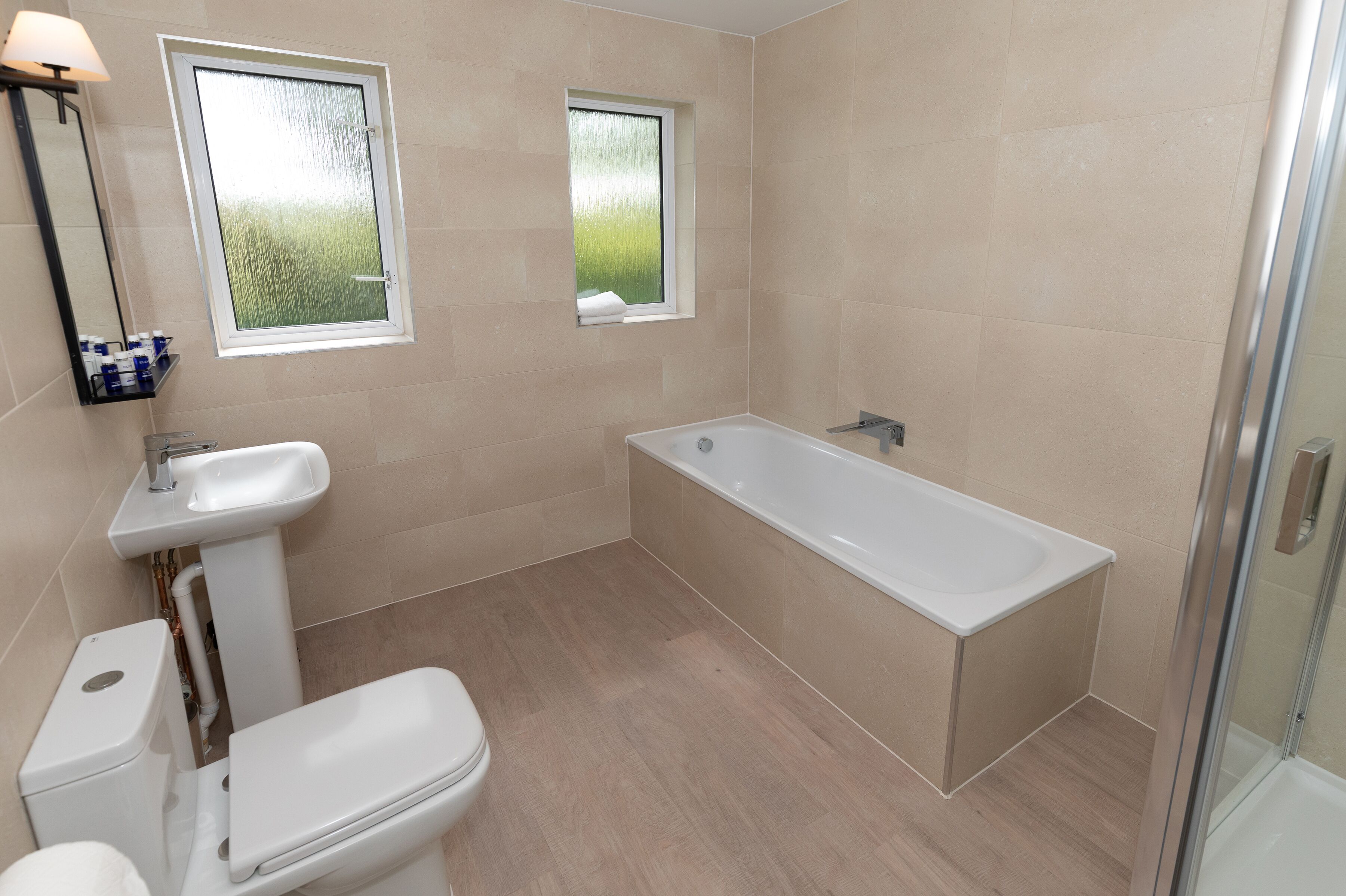 Un baño moderno con bañera, inodoro, lavabo y dos ventanas.