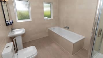 Un baño moderno con bañera, inodoro, lavabo y dos ventanas.