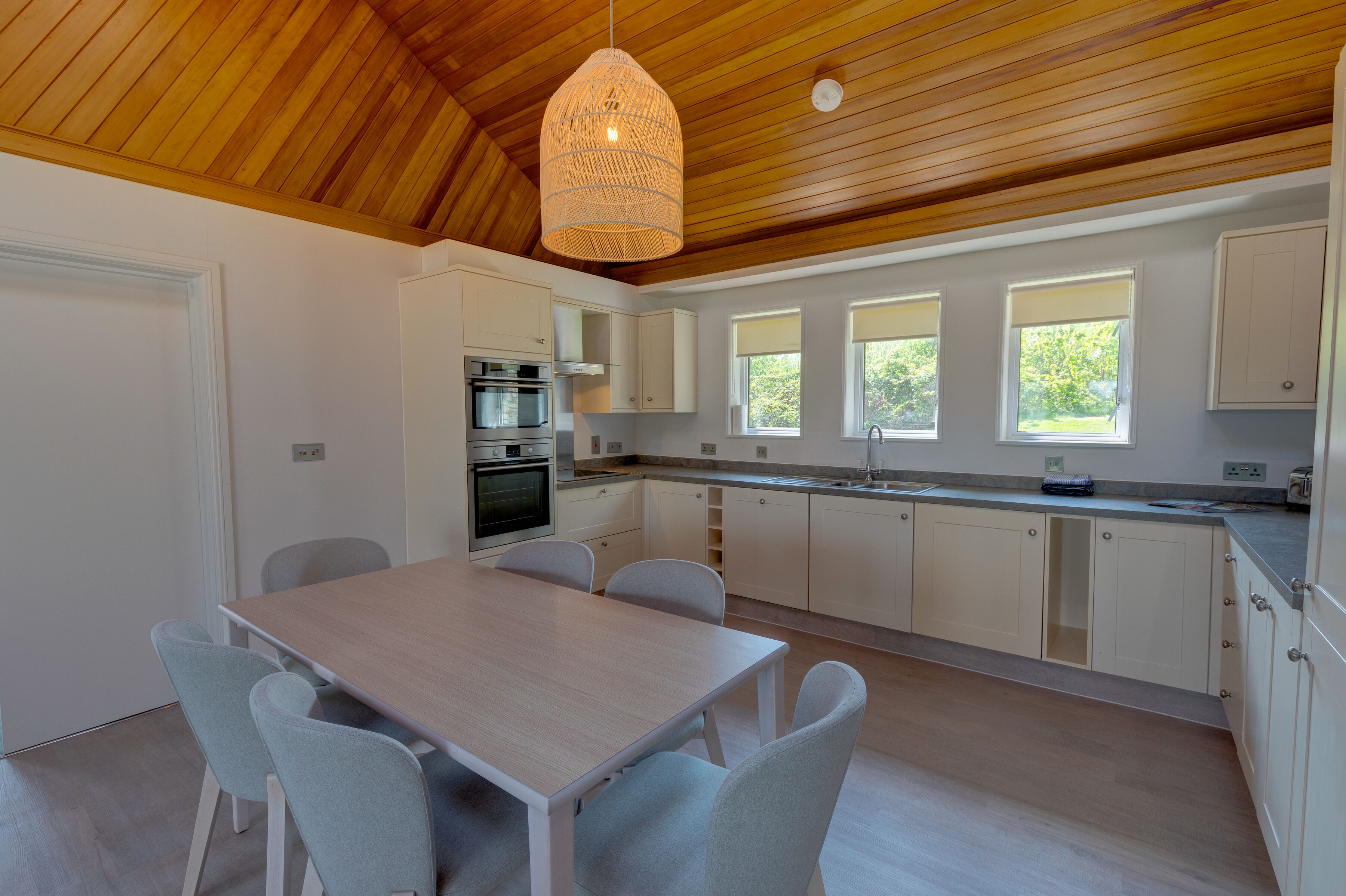 A modern kitchen with white cabinets, a wooden ceiling, and a dining area with a table and chairs.