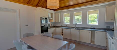 A modern kitchen with white cabinets, a wooden ceiling, and a dining area with a table and chairs.