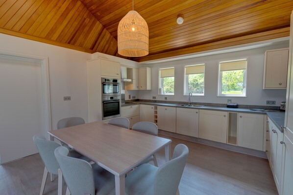 A modern kitchen with white cabinets, a wooden ceiling, and a dining area with a table and chairs.