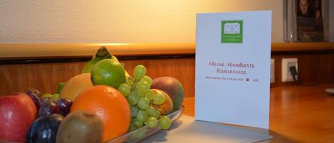 A fruit bowl with a variety of fruits and a hotel service card on a table.