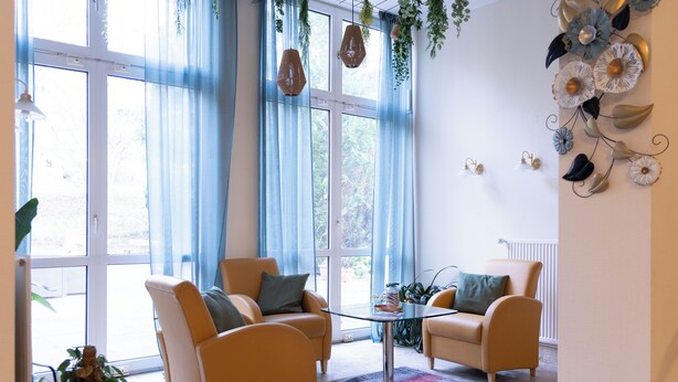A living room with two armchairs, a glass coffee table, and a large window with blue curtains. - Hotel Haus am Park (Bad Homburg v.d. Hoehe)