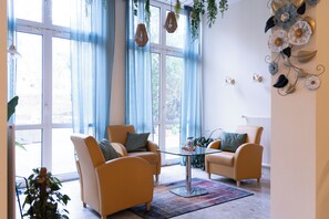 A living room with two armchairs, a glass coffee table, and a large window with blue curtains. - Hotel Haus am Park (Bad Homburg v.d. Hoehe)