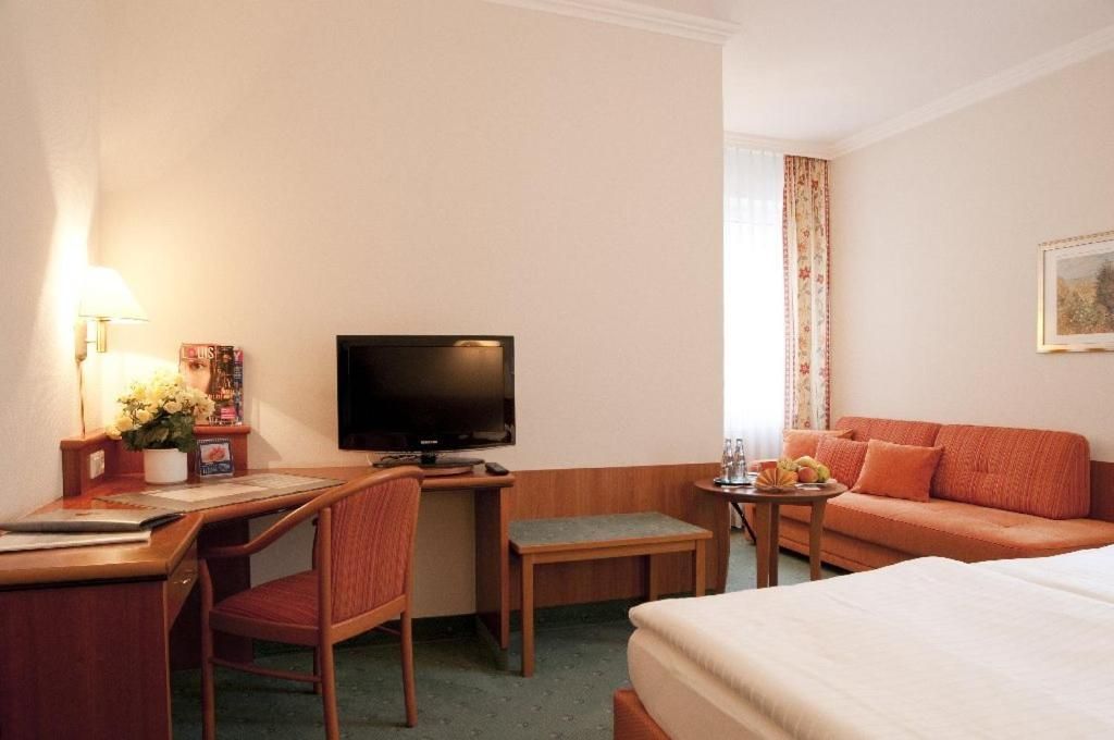 Ein Hotelzimmer mit einem Bett, einem Schreibtisch mit Stuhl, einem Fernseher und einem Sofa.