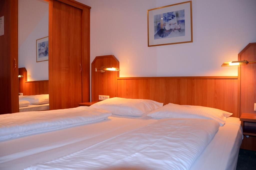 Habitación de hotel con dos camas, cabeceros de madera, lámparas de noche y un cuadro enmarcado en la pared.