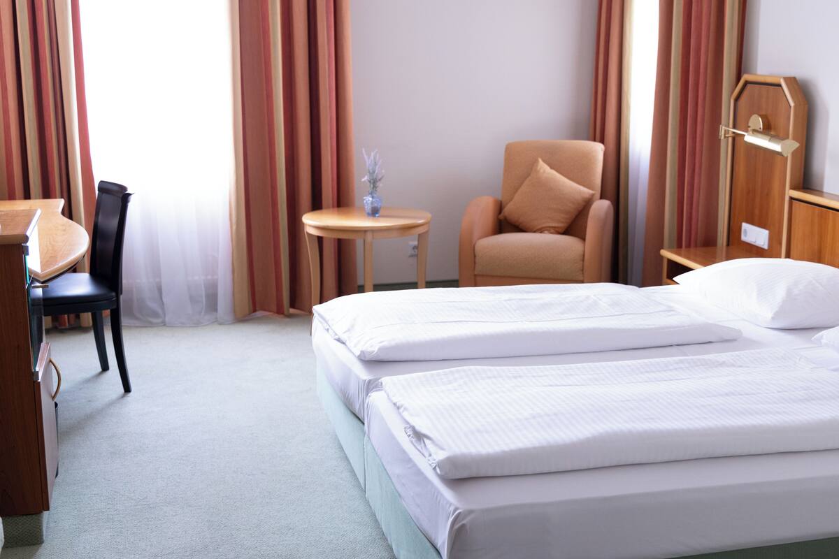 A hotel room with a bed, a desk, a chair, a small table, and curtains.