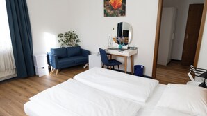 A bedroom with a bed, a desk with a chair, a blue sofa, a plant, and a door. - Hotel Haus am Park (Bad Homburg v.d. Hoehe)