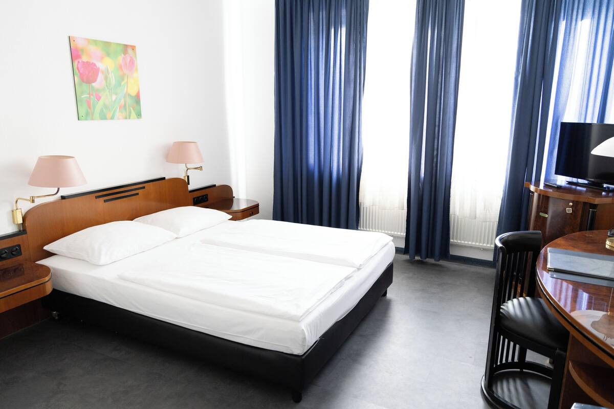 A hotel room with a double bed, bedside tables with lamps, a desk with a chair, and a television.