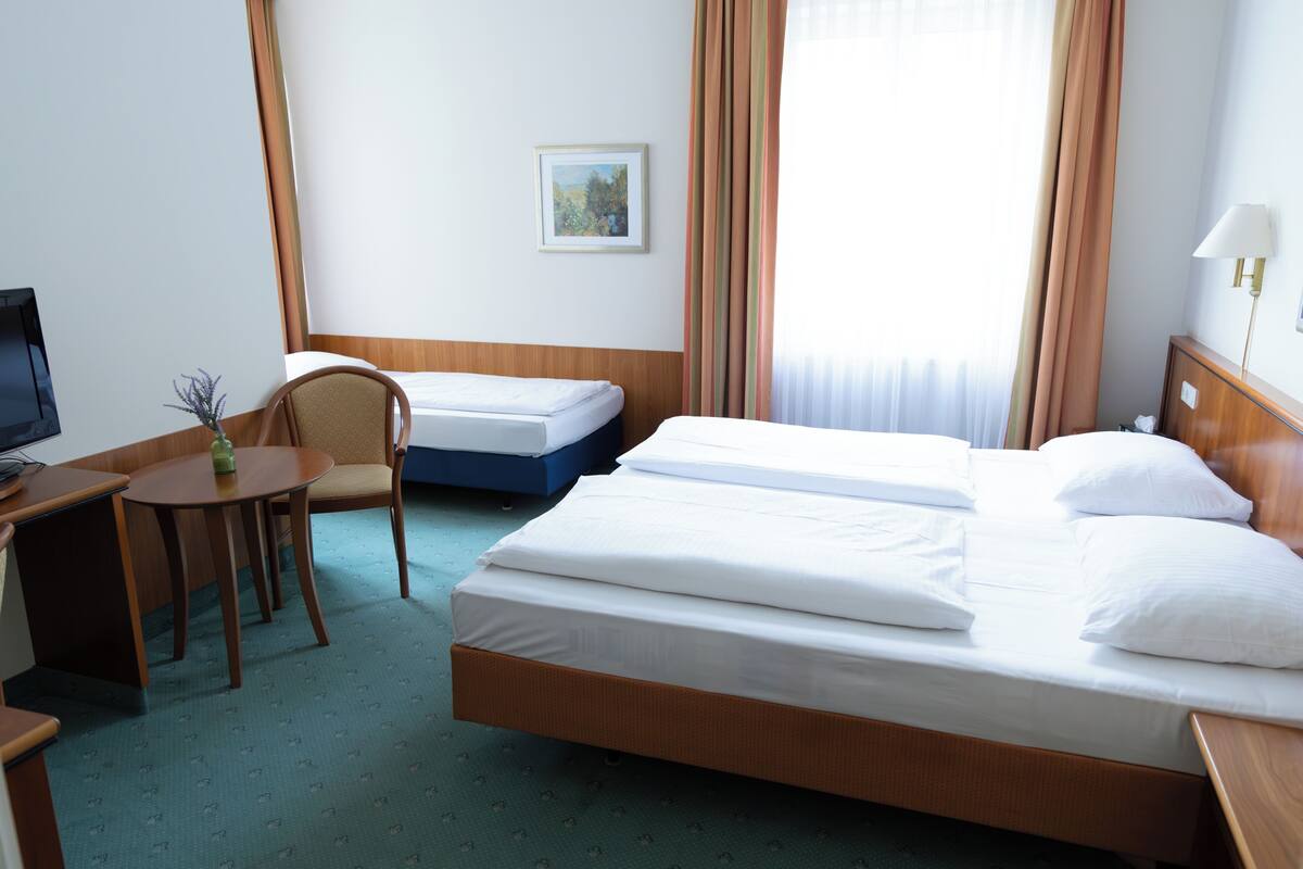 A hotel room with a large bed, a smaller bed, a desk with a chair, a TV, and a painting on the wall.