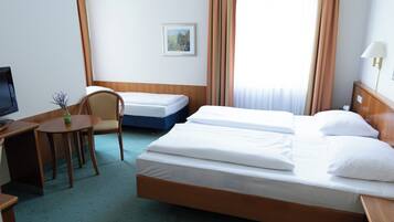 Una habitación de hotel con una cama grande, una cama más pequeña, un escritorio con una silla, un televisor y un cuadro en la pared.