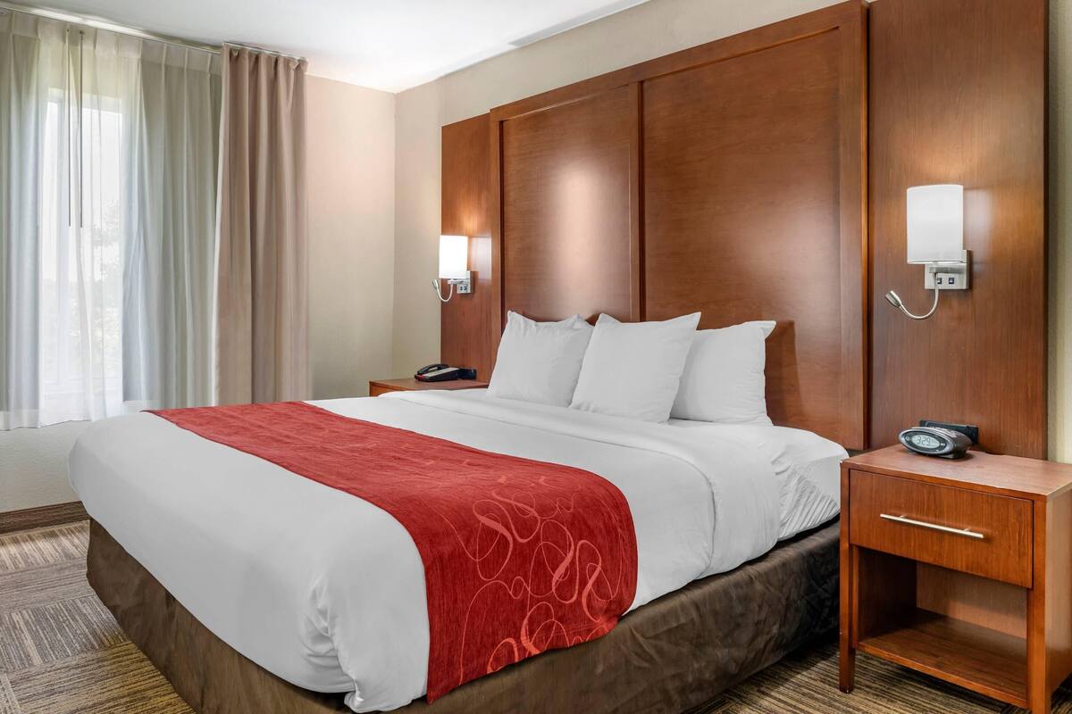 Une chambre d’hôtel avec un grand lit, une tête de lit en bois, une table de chevet avec un téléphone et une lampe fixée au mur.