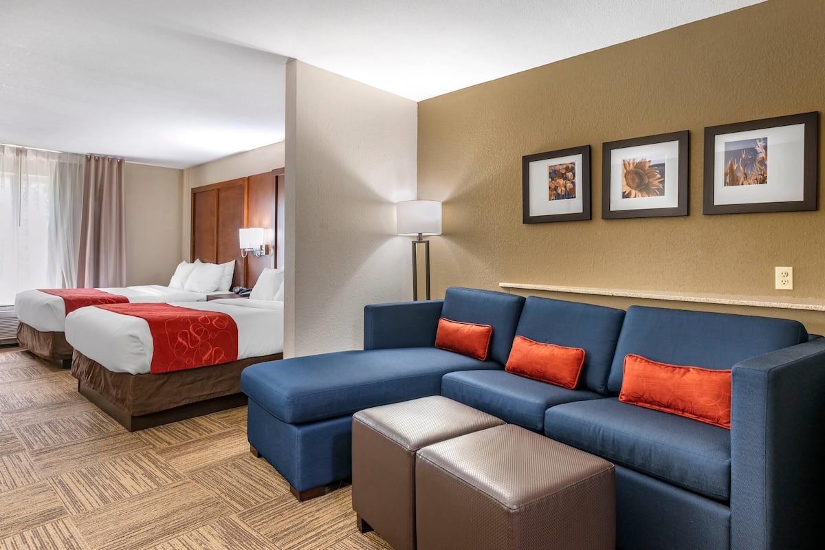 Une chambre d’hôtel avec deux lits, un canapé bleu et une lampe.