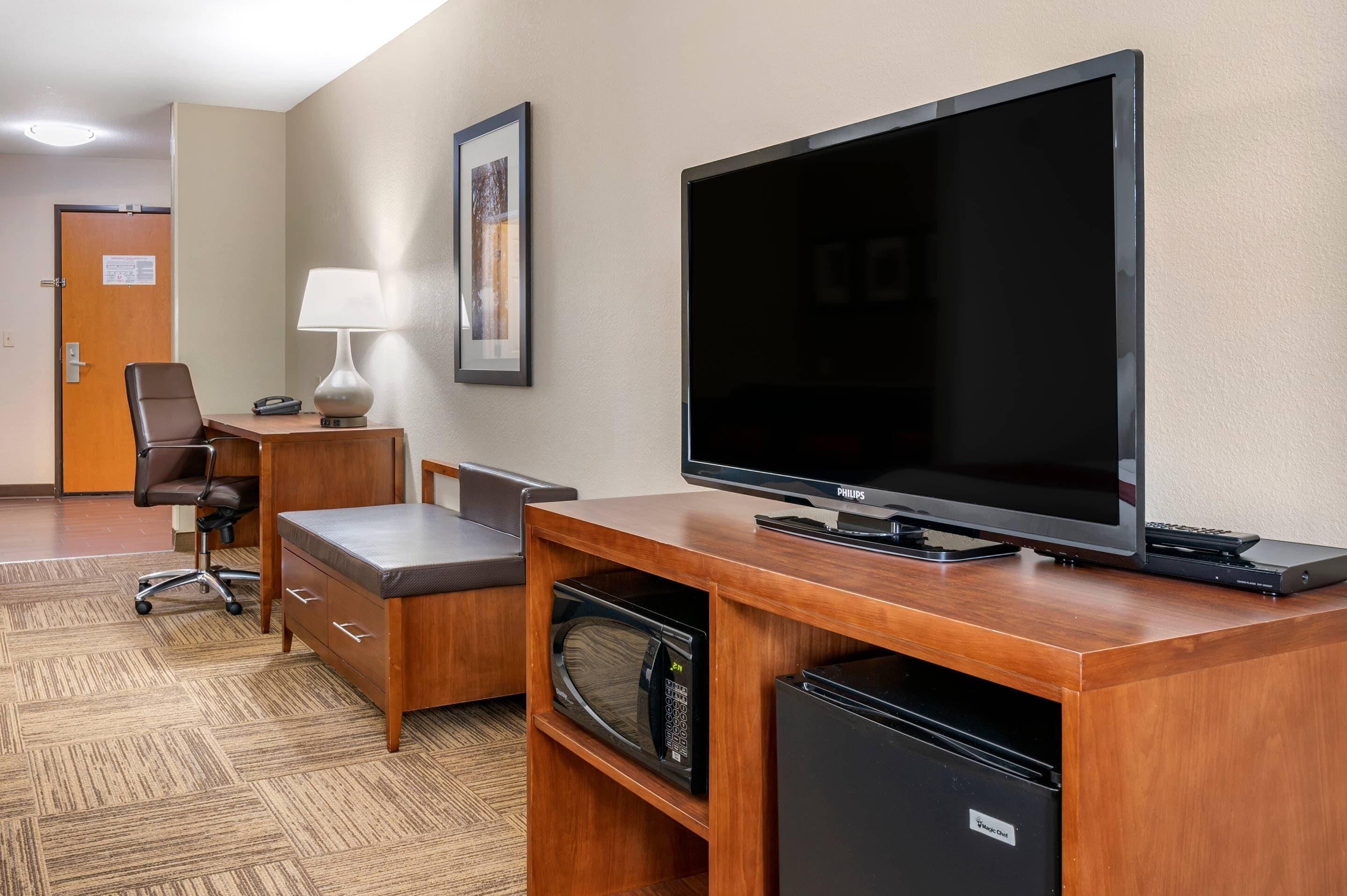 Hotelkamer met een houten bureau, een flatscreen televisie, een stoel, een lamp, een magnetron en een minibar.