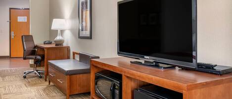 Hotelkamer met een houten bureau, een flatscreen televisie, een stoel, een lamp, een magnetron en een minibar.