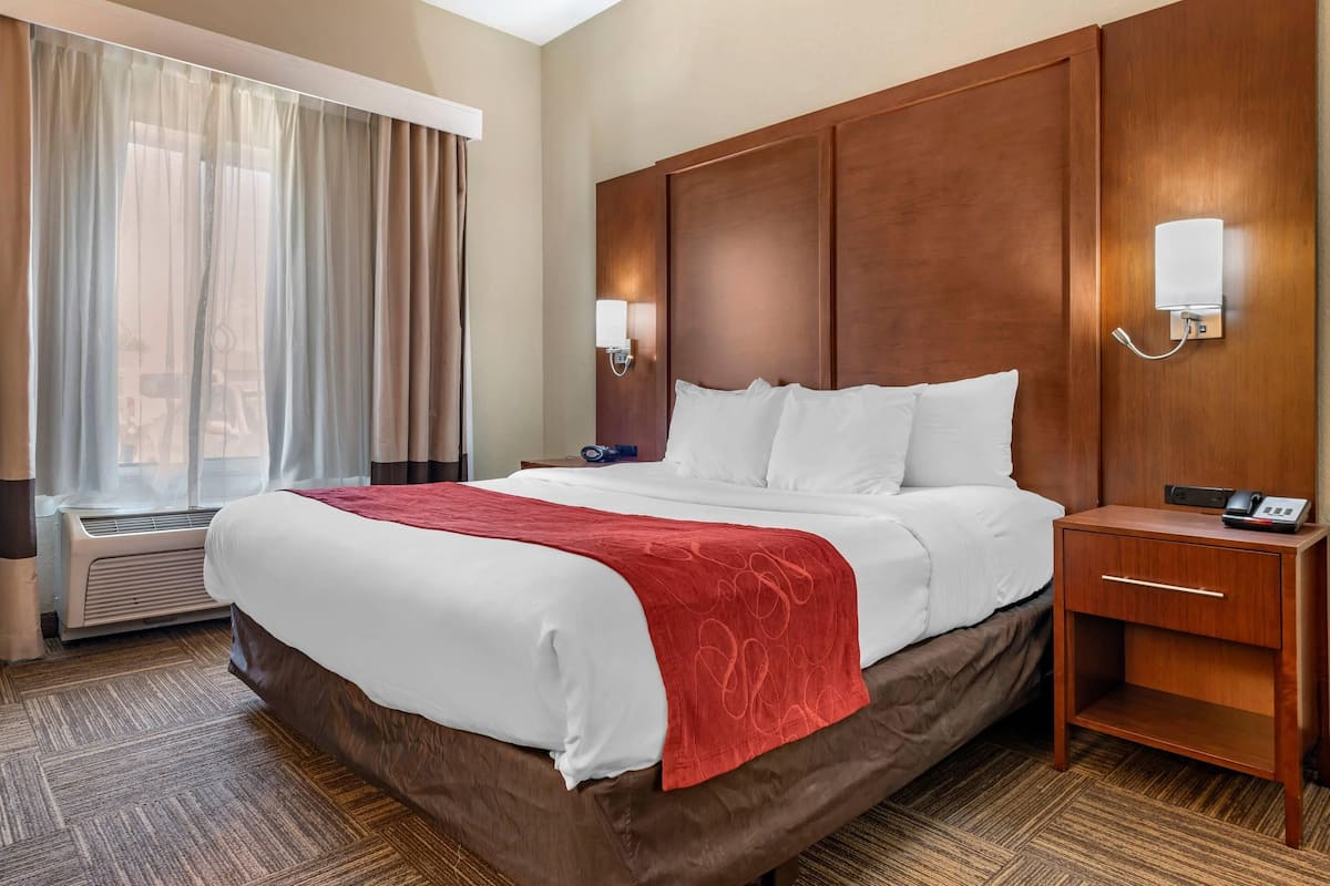 Une chambre d’hôtel avec un grand lit, une tête de lit en bois, une table de chevet avec un téléphone et une fenêtre avec des rideaux.