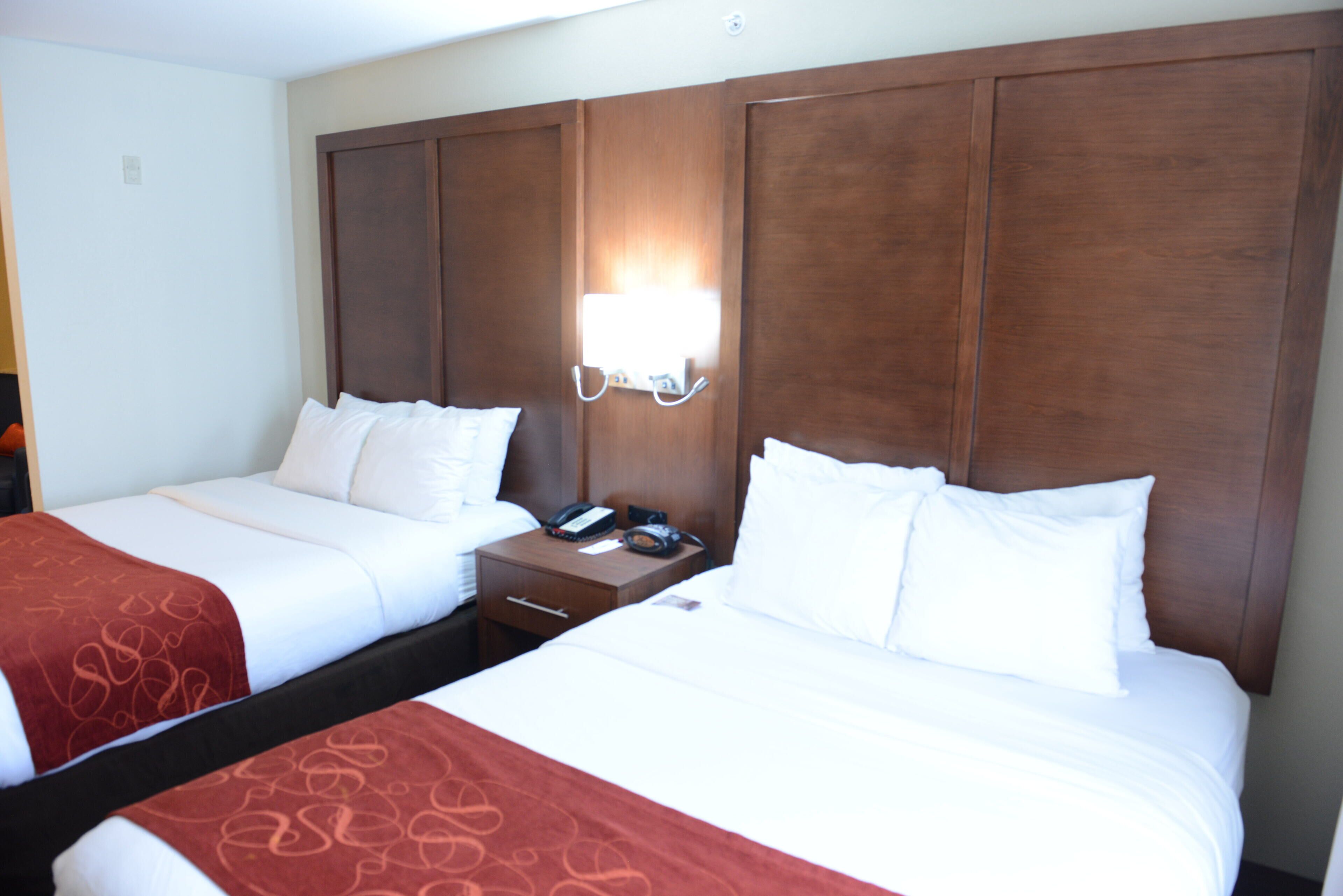 A hotel room with two beds, a nightstand with a phone, and a wall-mounted light.