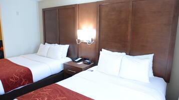 A hotel room with two beds, a nightstand with a phone, and a wall-mounted light.