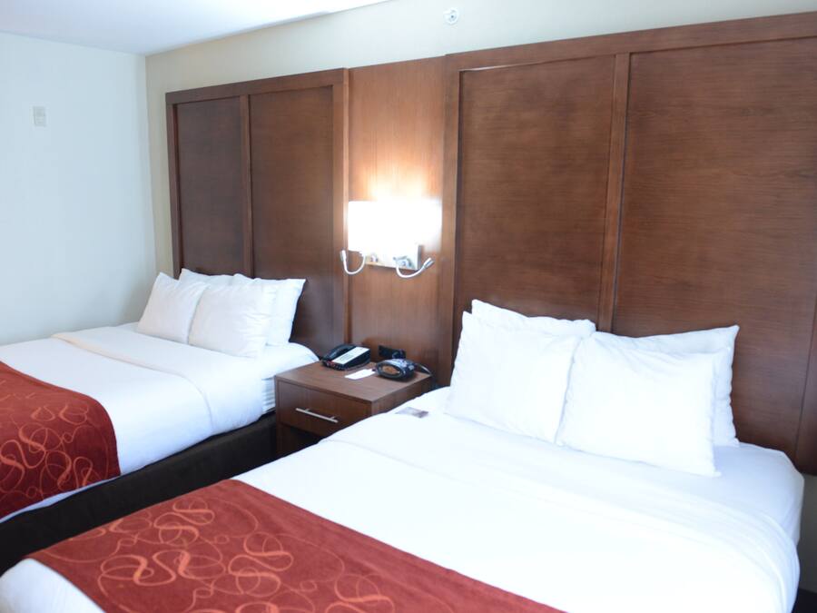 A hotel room with two beds, a nightstand with a phone, and a wall-mounted light.