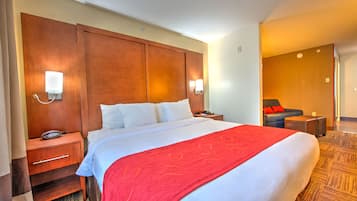 Quarto de hotel com uma cama grande, cabeceira de madeira, duas mesas de cabeceira, um cobertor vermelho e piso coberto por carpete.