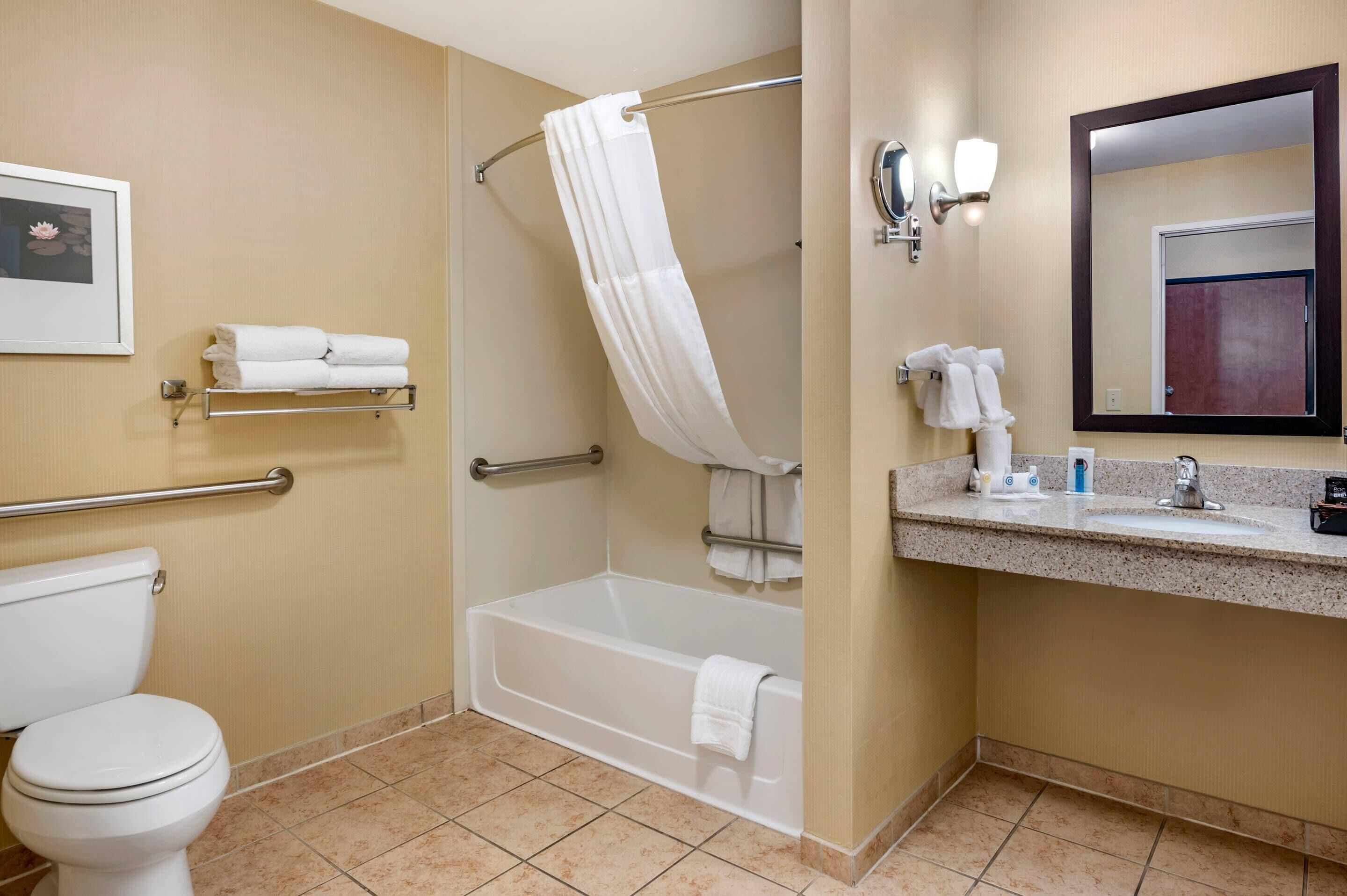 A bathroom with a toilet, a bathtub, a shower with a curtain, a sink with a mirror, and towel racks.