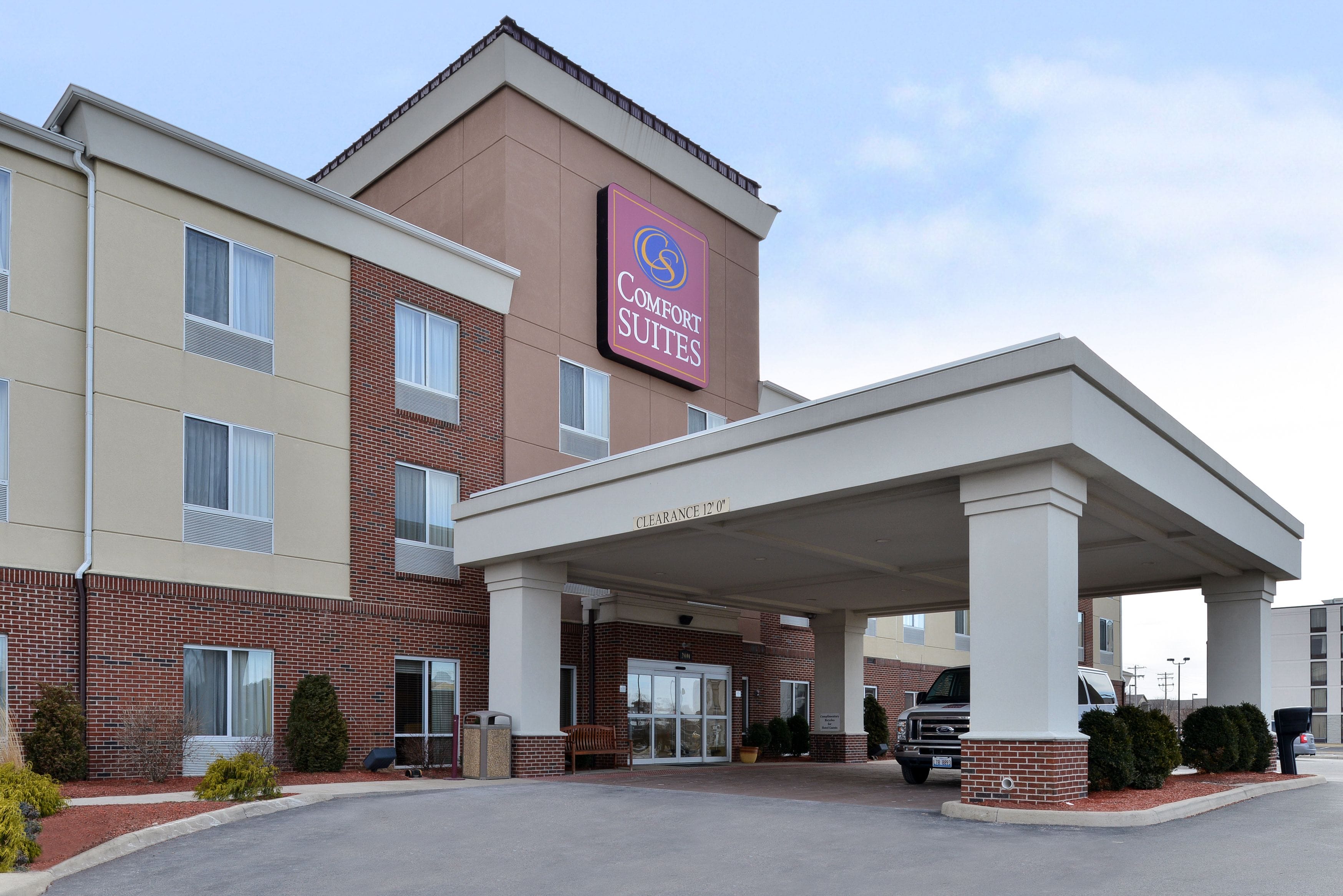 Un hotel con un letrero que dice "Comfort Suites" y una entrada cubierta con una altura libre de 3.6 metros.