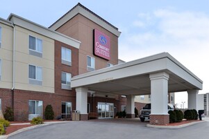 Un hotel con un letrero que dice "Comfort Suites" y una entrada cubierta con una altura libre de 3.6 metros.
