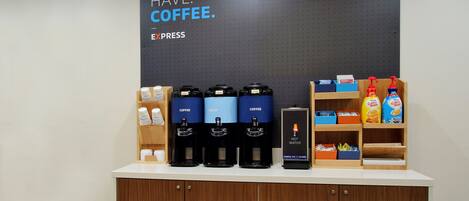 A coffee station with multiple coffee dispensers, a hot water station, and a variety of coffee products on shelves.