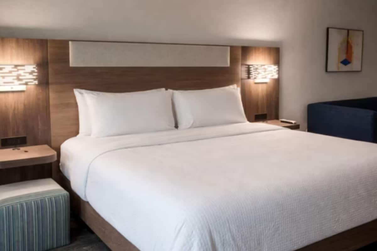 A hotel room with a large bed, two bedside tables, a nightstand, a chair, and wall-mounted lighting.