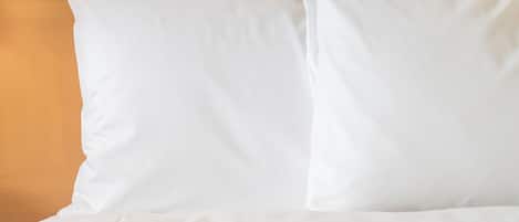 A bed with white bedding and pillows against a wooden headboard.