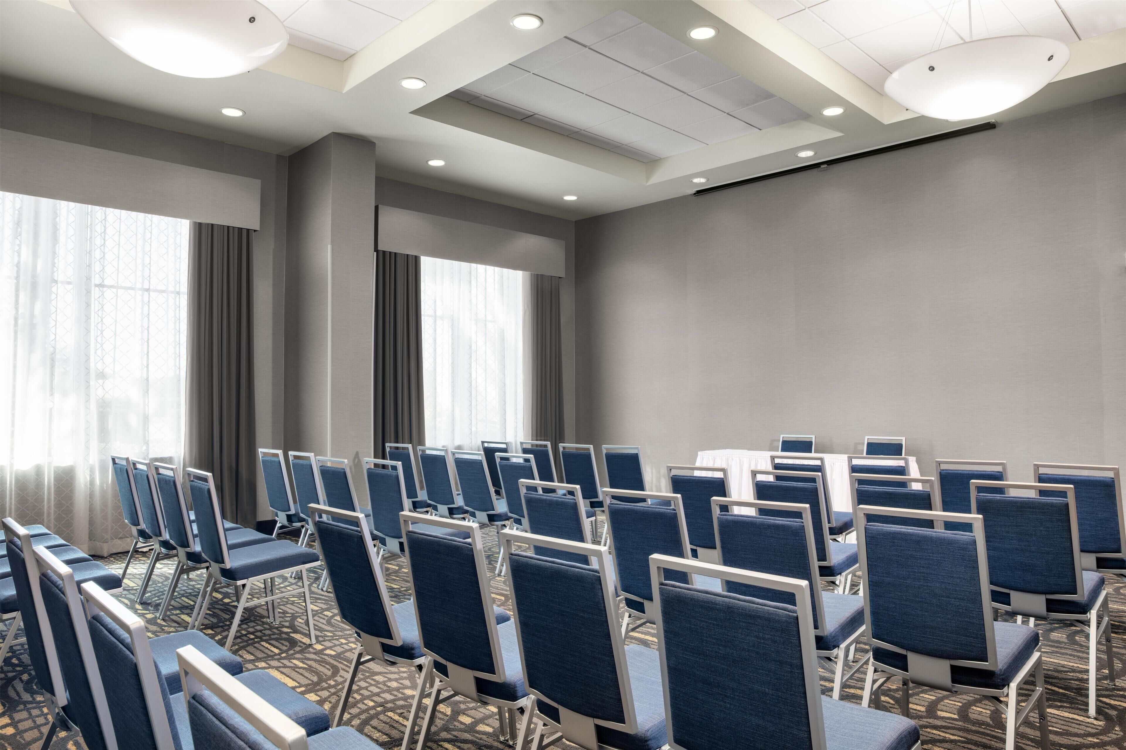 A conference room with rows of chairs, a large table, and a projector screen.