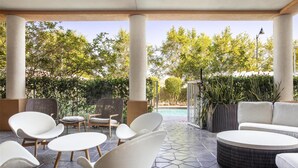 A covered outdoor seating area with modern chairs and a round table, surrounded by greenery and a view of a swimming pool. - Hampton Inn & Suites Homestead Miami South (Homestead)