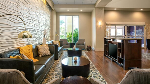 A modern living room with a sofa, two round coffee tables, a TV, and a patterned wall. - Hampton Inn & Suites Homestead Miami South (Homestead)