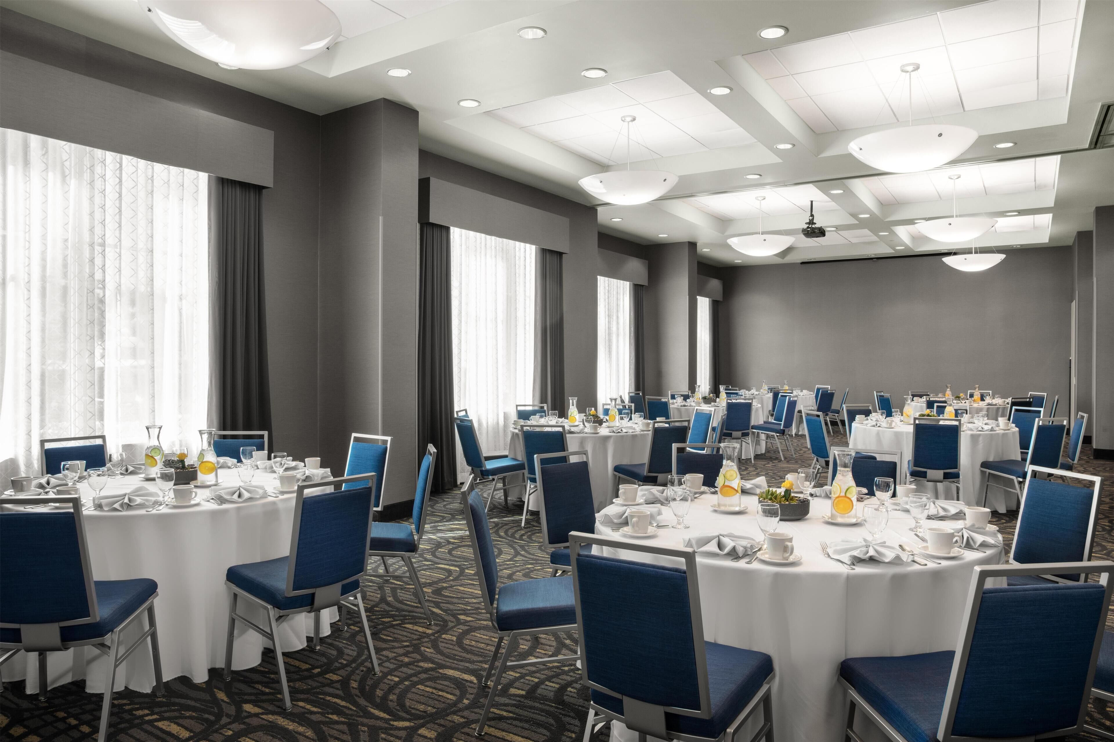 A conference room with round tables, blue chairs, and white tablecloths.