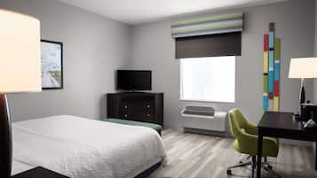 Habitación de hotel con cama, escritorio, silla, televisor y ventana con persianas.
