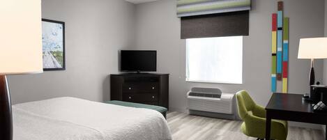 Habitación de hotel con cama, escritorio, silla, televisor y ventana con persianas.