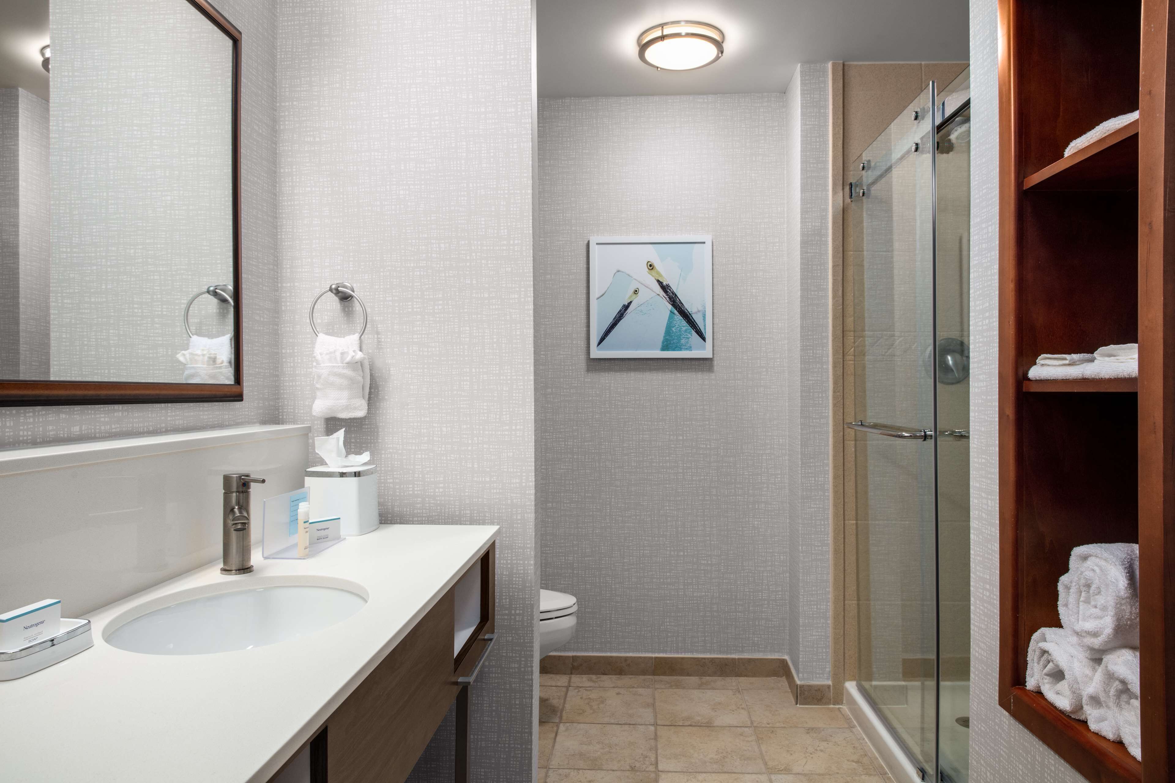 Un baño moderno con un espejo grande, un lavamanos, un inodoro y una ducha con mampara de vidrio.