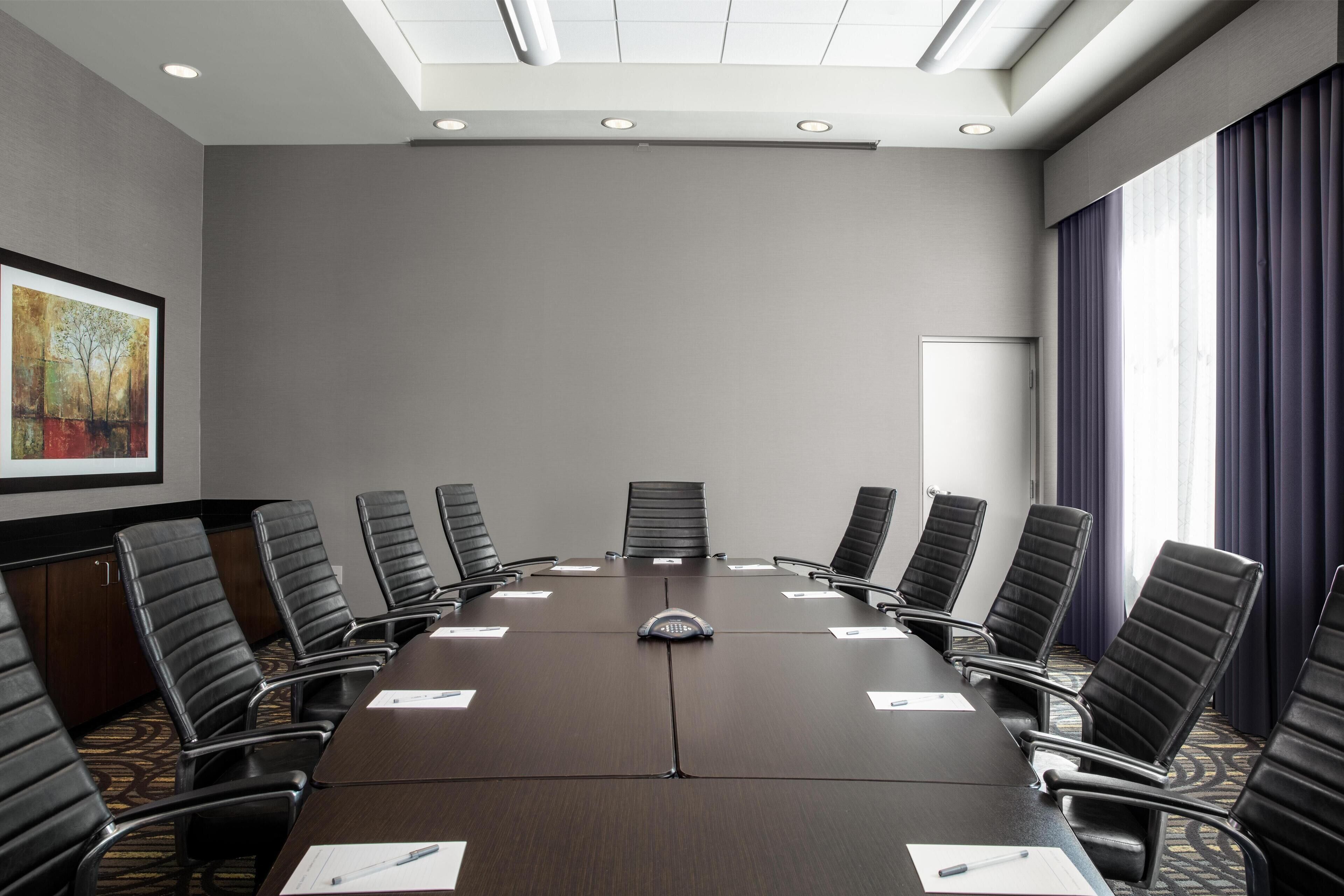 A conference room with a long table, black chairs, a whiteboard, and a painting on the wall.
