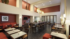 Ein geräumiges Restaurant mit mehreren Essbereichen, darunter Sitzecken und Tische. An den Wänden stehen dekorative Vasen und es gibt eine lange Theke mit Stühlen.