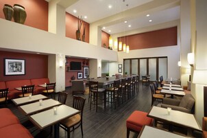 Un restaurante amplio con varias zonas de comedor, incluidas cabinas y mesas. Hay jarrones decorativos en las paredes y una larga barra con sillas.
