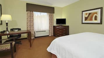 Habitación de hotel con cama, escritorio con silla, televisor y un cuadro en la pared.
